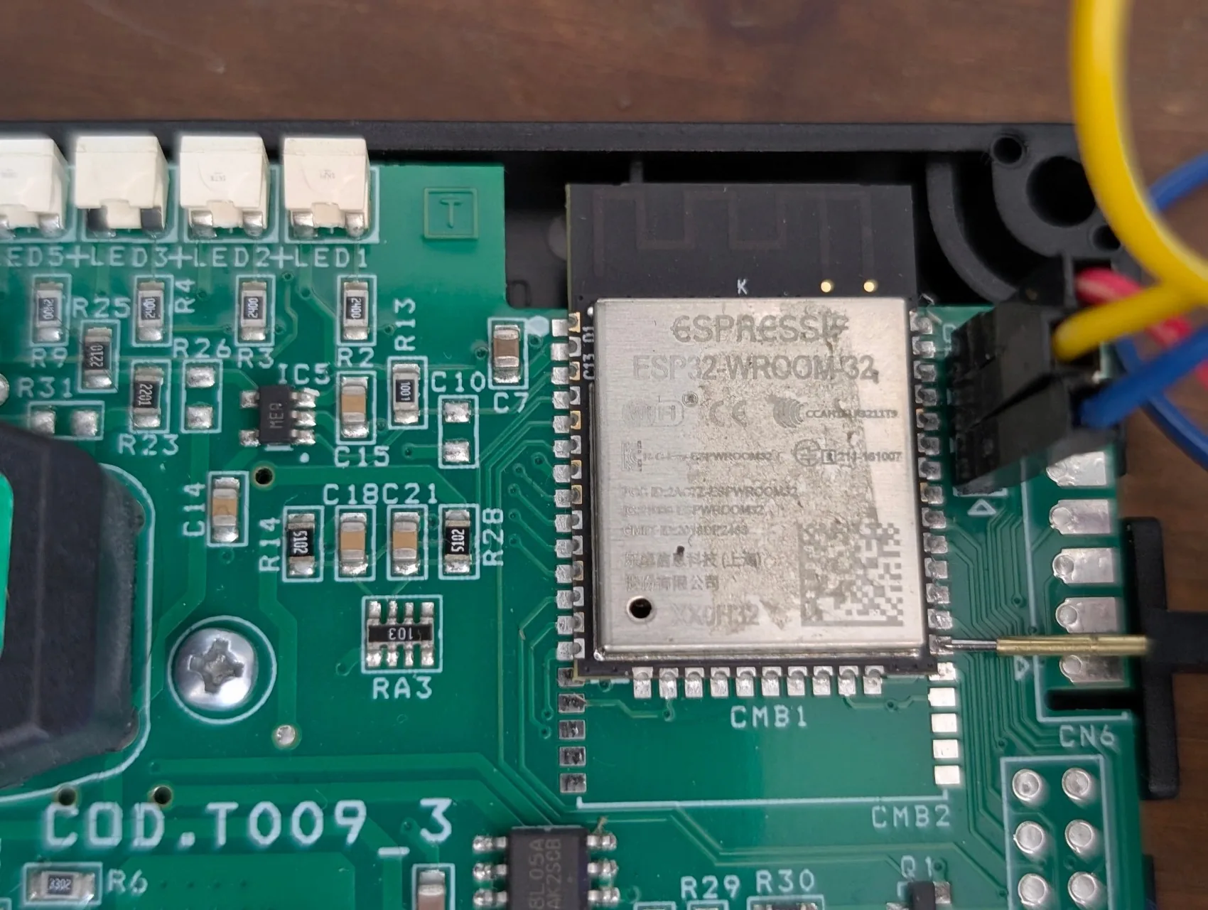 Vue macro sur l'ESP32-WROOM32 : broche dupont mâle du fil jaune posée directement contre le pad IO0 (=côté gauche de la puce), fil qui redescend vers CN6 pin 1 GND en bas à gauche, câblage UART CN5 rouge/jaune/bleu visible en dessous