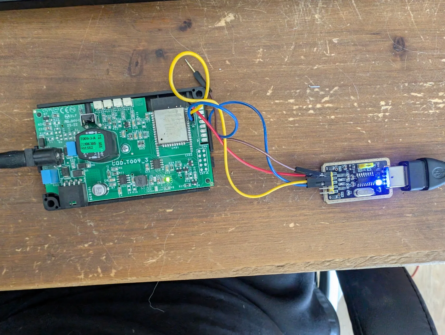 Setup complet en cours de dump : module Extraflame à gauche avec jack d'alim branché, CH340G à droite en USB-C, 3 dupont rouge (GND) / jaune (TX module = RXD CH340G) / bleu (RX module = TXD CH340G) qui relient les deux ; LED verte du module allumée = alim OK