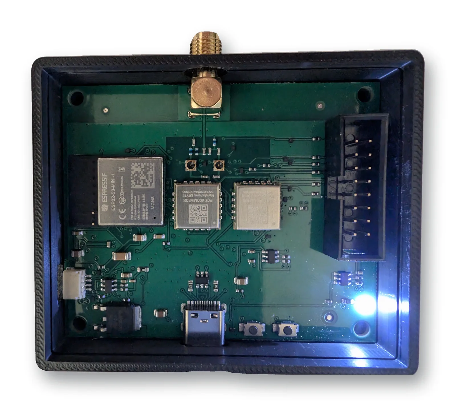 La première carte EVT numéro 0001, sous tension dans son boîtier imprimé : la carte vissée sur ses plots, l'embase SMA qui sort par le haut, le mikroBUS traversant à droite, l'USB-C et les deux boutons en bas, la LED bleue allumée